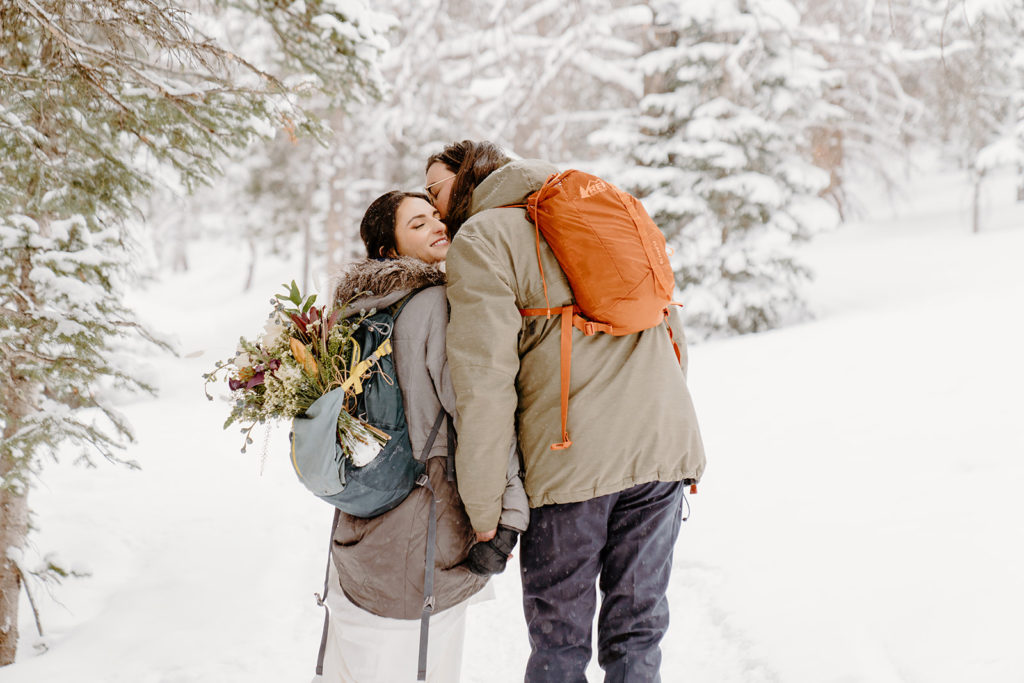 man kissing woman's cheek holding hands in the snow
