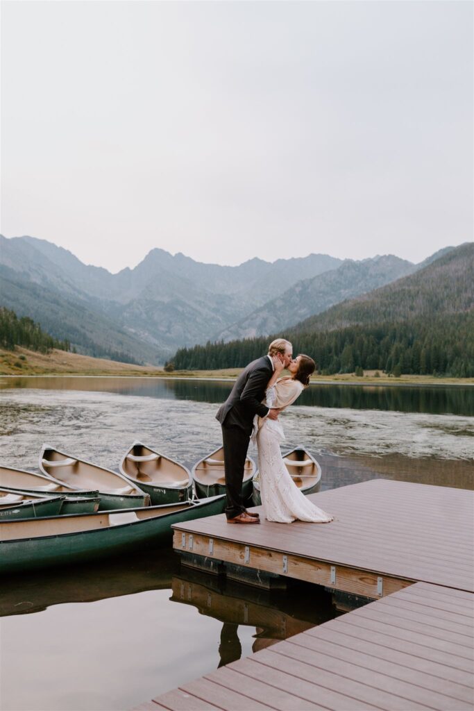 man and woman kissing on dock surrounded by mountains