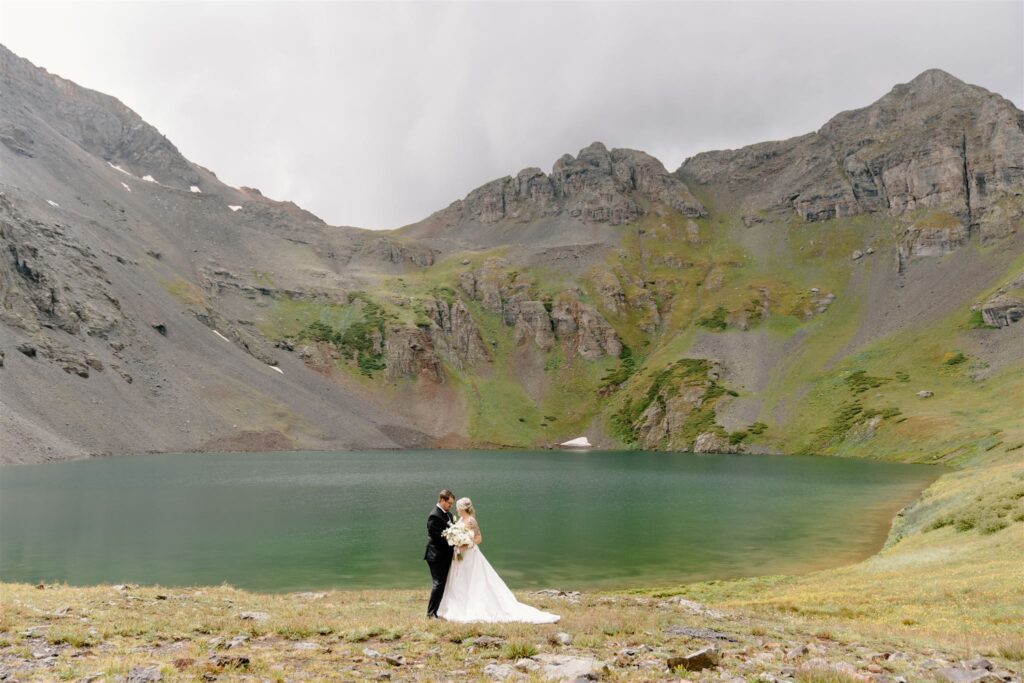 bride and groom standing in front of an alpine lake
