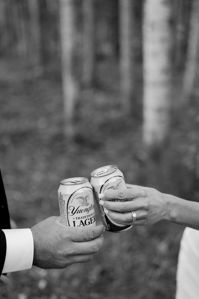 Bride and groom cheers with a beer in the forest to celebrate their wedding in Telluride