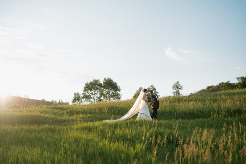 Bride and groom walk hand in hand through a Colorado meadow at sunset