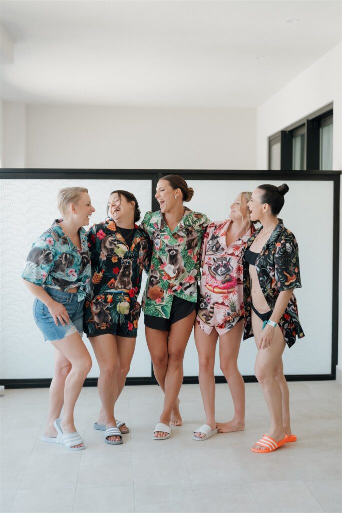 Bride and bridesmaids laugh together in their matching tropical raccoon shirts